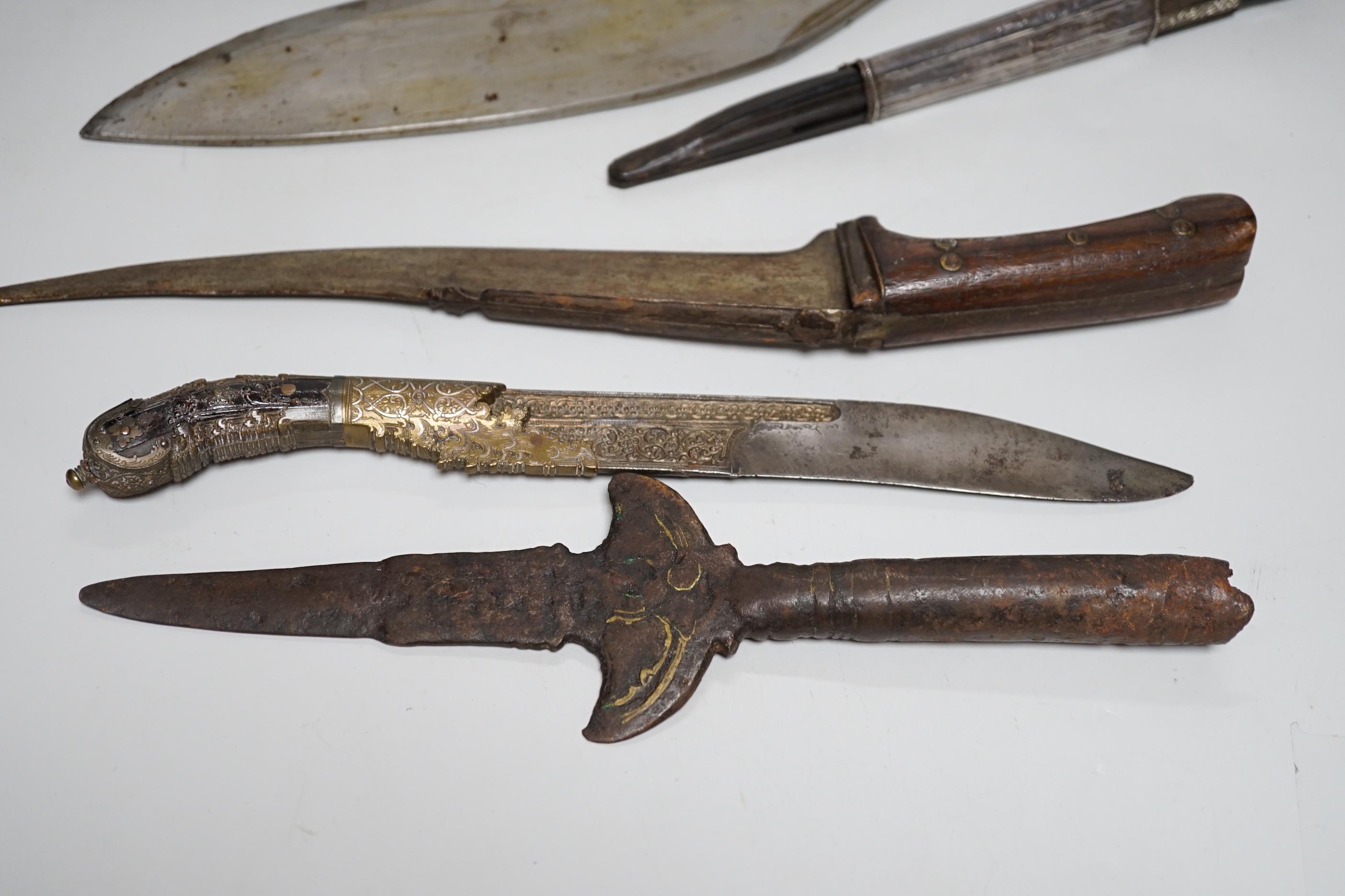 Two Sinhalese daggers and a kukri, a silver inlaid Kirichchiya dagger, together with another in a scabbard with a long pin, another dagger with a wooden handle and a head of a brass inlaid iron pole arm, longest 43cm